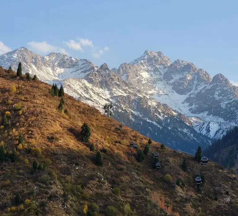 Snowy peaks above an autumn slope with a cable car
